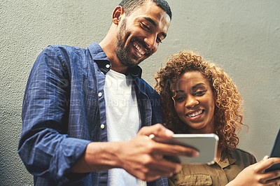 Buy stock photo Smiling young couple looking, laughing and holding phone together showing a funny social media app. Friends sharing a gossip news article post online. Guy looking at internet web content with girl