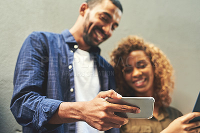 Buy stock photo Shot of a young couple looking at a smartphone together outside