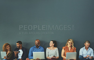 Buy stock photo Group of happy business people sharing information on wireless technology in a row at an office together. Corporate professionals sitting and talking using devices in a waiting room together at work