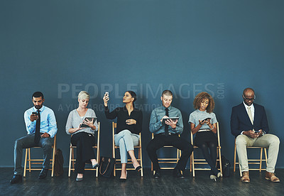 Buy stock photo Shot of a group of business people using their smart devices while waiting to be interview