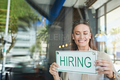 Buy stock photo Shot of a young entrepreneur holding a “hiring” sign in her business