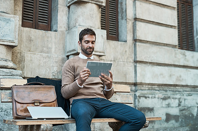 Buy stock photo Full length shot of a handsome businessman using his tablet while sitting on a bench in town