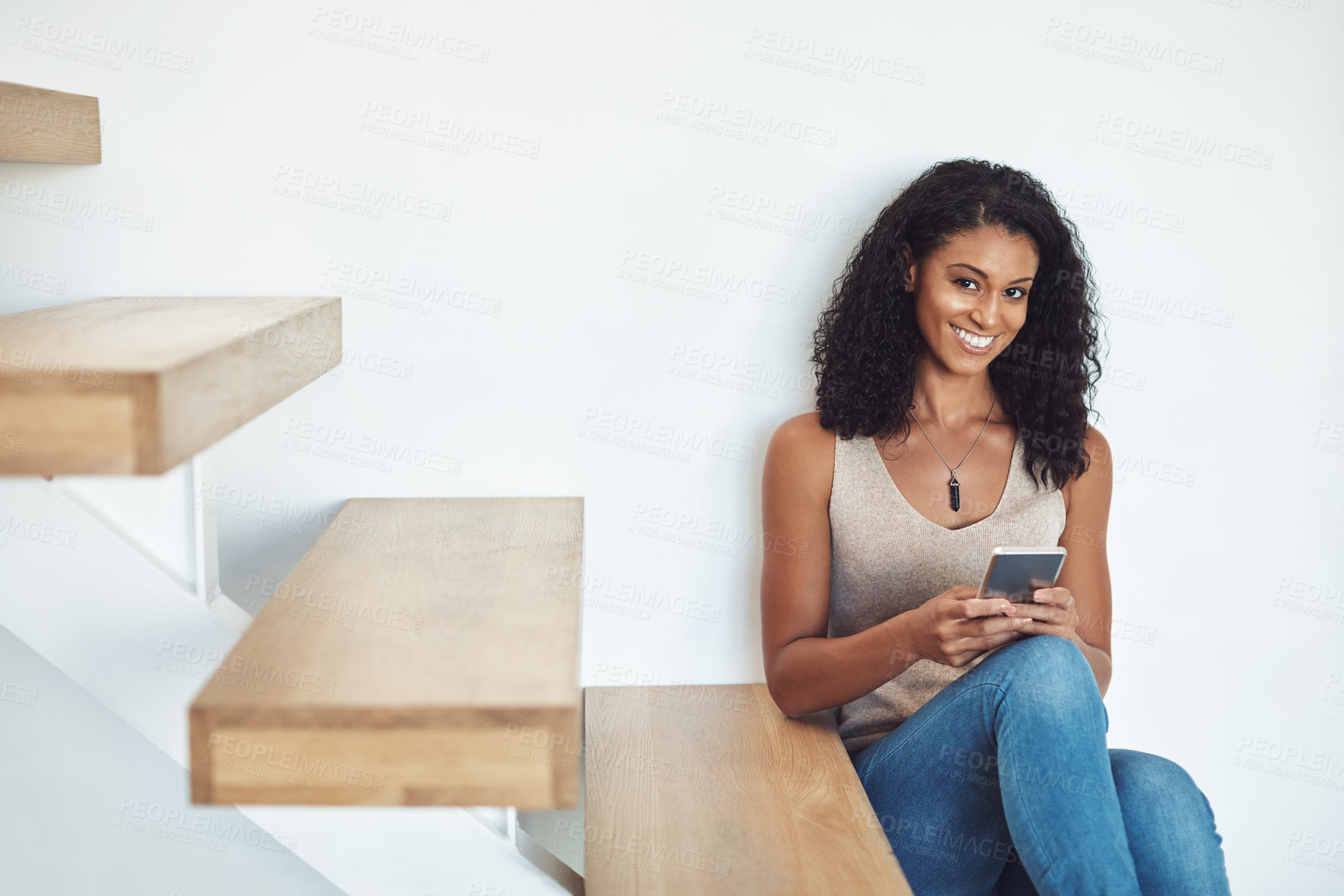 Buy stock photo Happy woman typing on phone, texting a message on social media or browsing the internet while sitting on stairs at home. Portrait of a confident, beautiful and female relaxing on wooden steps.