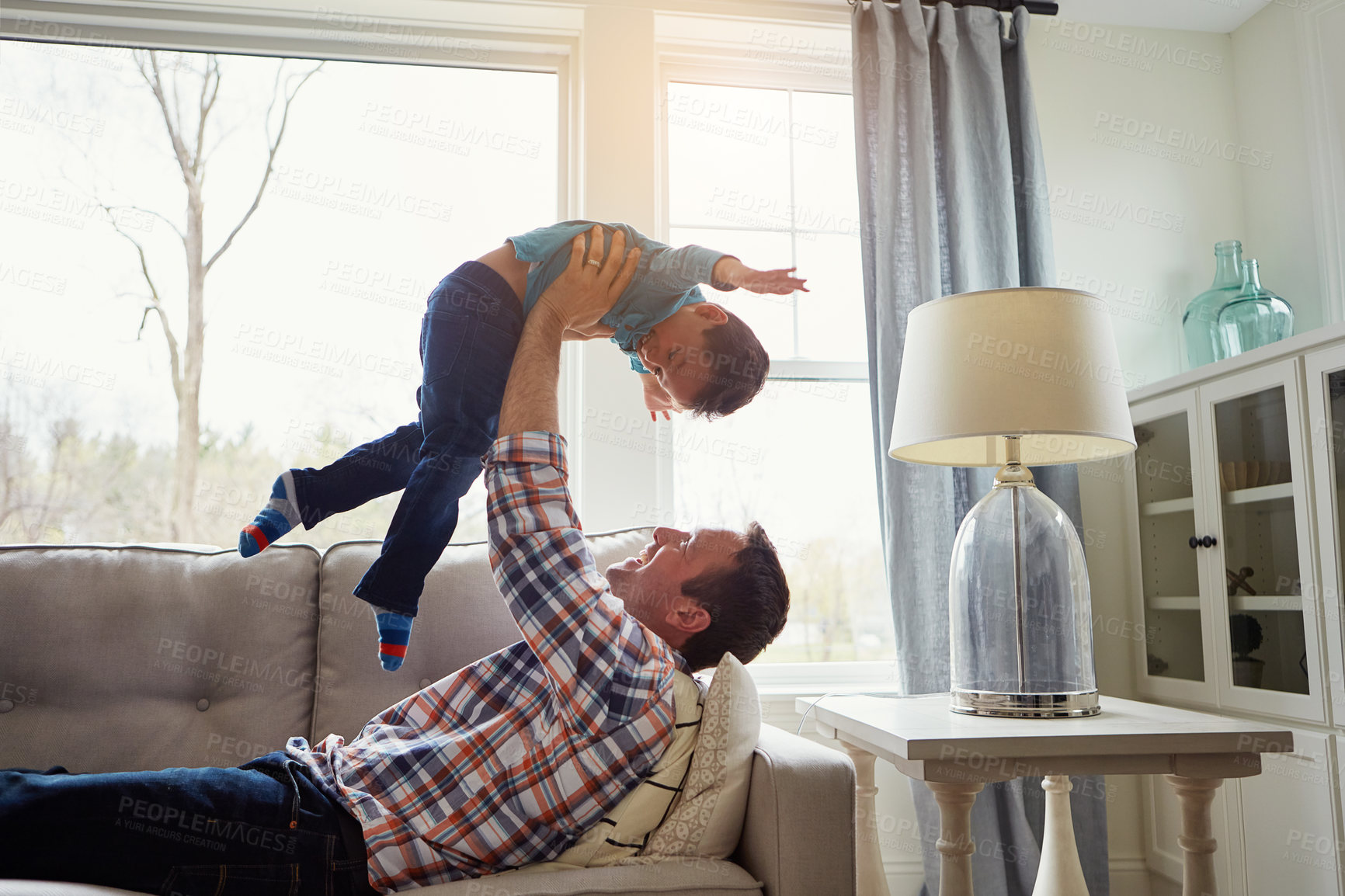 Buy stock photo Father, child and happy on couch for airplane game, playful and bonding with care, love and laughing in house. Dad, boy and lifting for plane, connection and flight on sofa in lounge at family home