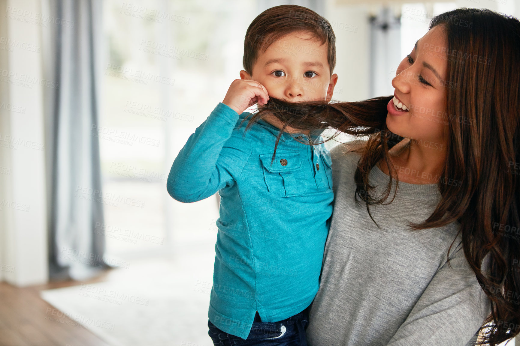 Buy stock photo Shot of a cute little boy playfully covering his mouth with his mother’s hair