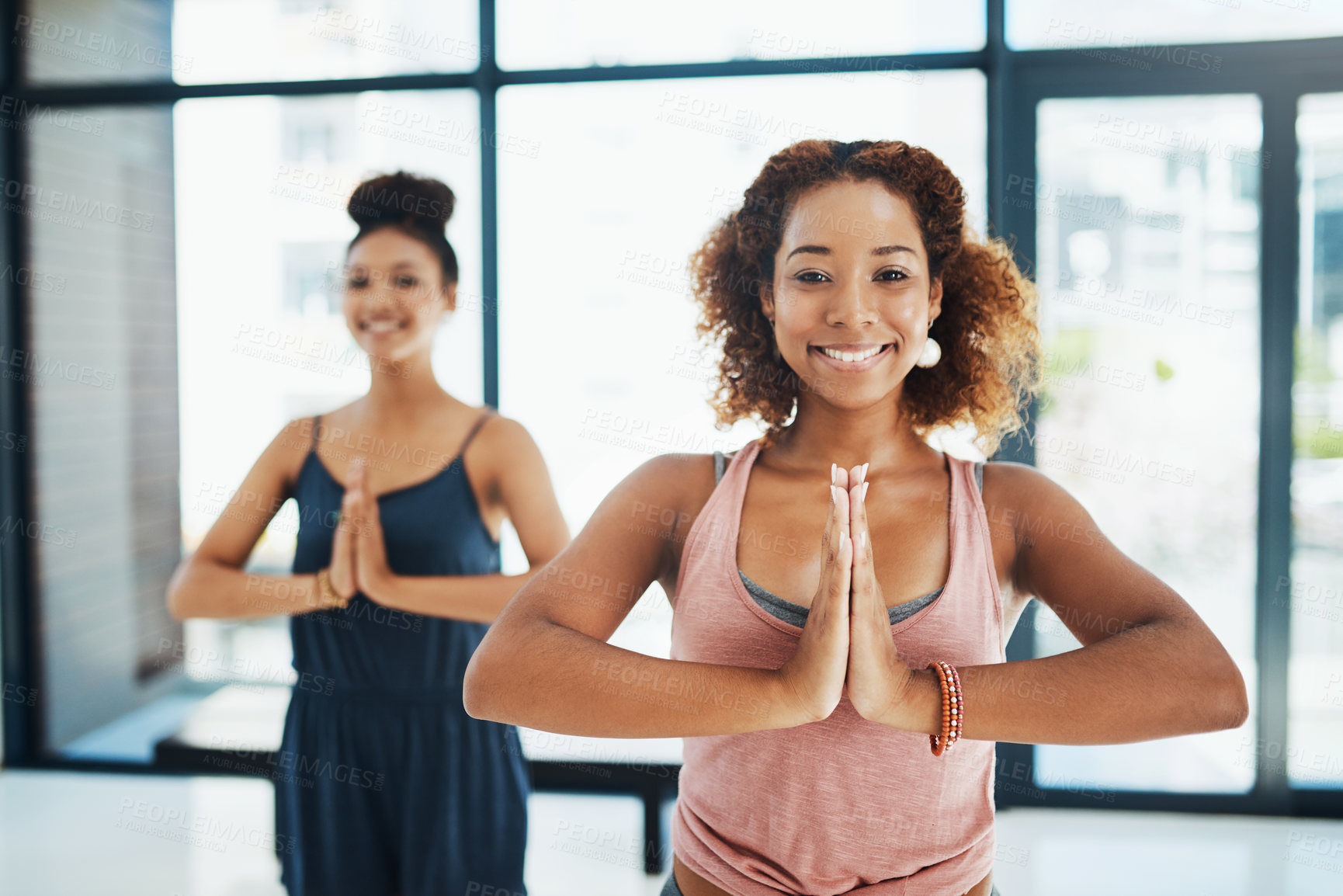 Buy stock photo Portrait shot of two young fit women standing and doing a yoga pose while looking at the camera inside of a studio