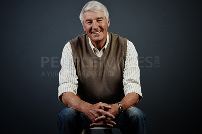 Buy stock photo Studio portrait of a handsome mature man sitting on a stool against a dark background