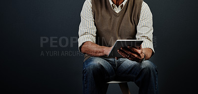 Buy stock photo Studio shot of an unrecognizable man using a tablet while sitting on a wooden stool against a dark background
