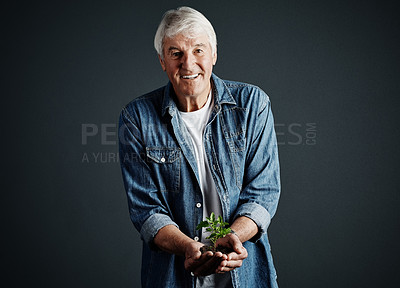 Buy stock photo Studio portrait of a handsome mature man holding a budding plant against a dark background