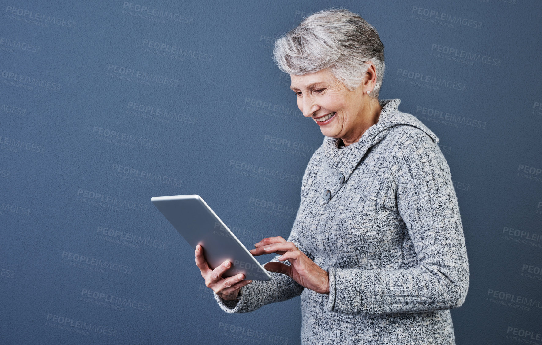 Buy stock photo Studio shot of an cheerful elderly woman standing and using a tablet