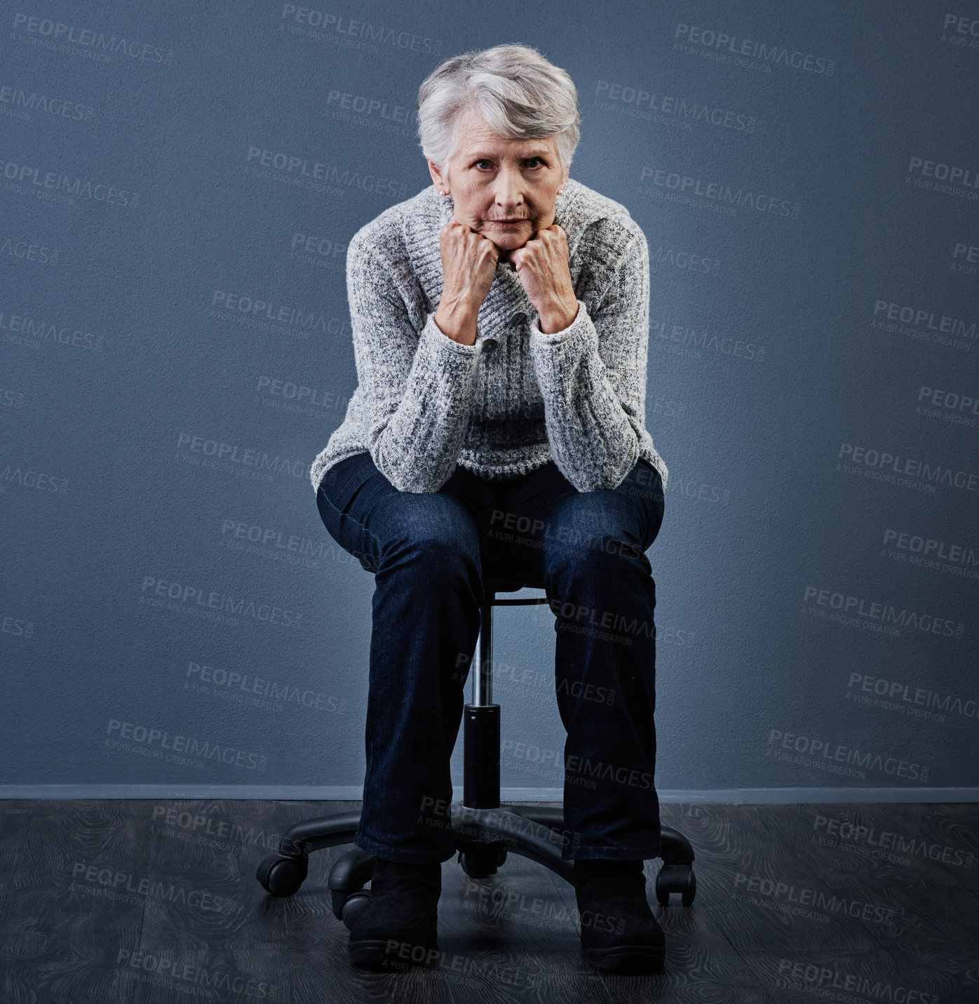 Buy stock photo Studio shot of an elderly woman sitting with her hands under her chin while looking at the camera