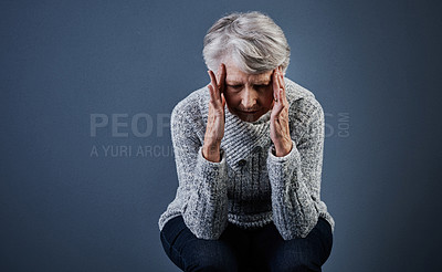 Buy stock photo Studio shot of a elderly woman sitting with her hands touching the sides of her head while looking down