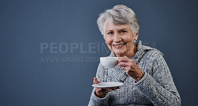 Buy stock photo Studio shot of a cheerful elderly woman sitting down and enjoying a cup of tea while looking at the camera