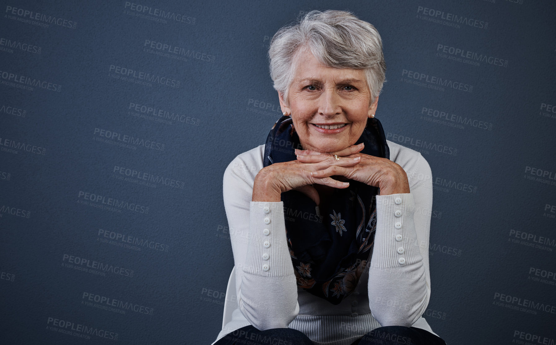 Buy stock photo Studio shot of cheerful elderly woman sitting with her hands under her chin while looking at the camera