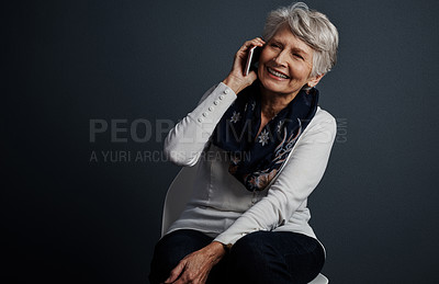 Buy stock photo Studio shot of a cheerful elderly woman sitting down and talking on her cellphone