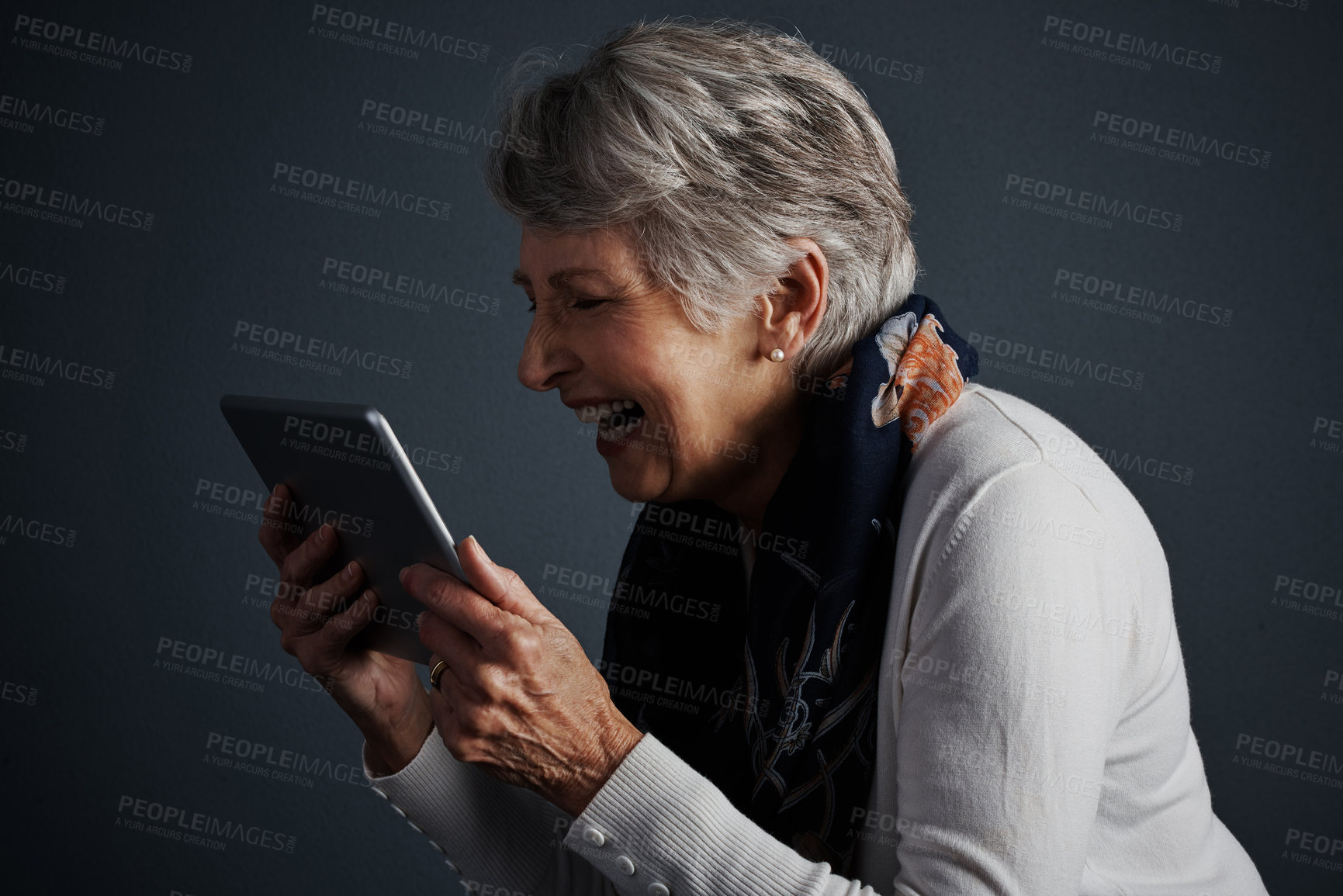 Buy stock photo Studio shot of a cheerful elderly woman standing and looking straight into her tablet with a smile