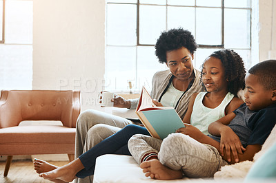Buy stock photo Shot of a little brother and sister reading a book while their mother watches at home