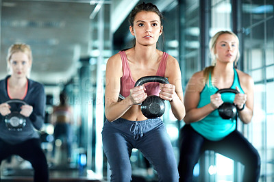 Buy stock photo Shot of three attractive young women working out with kettle bells in the gym