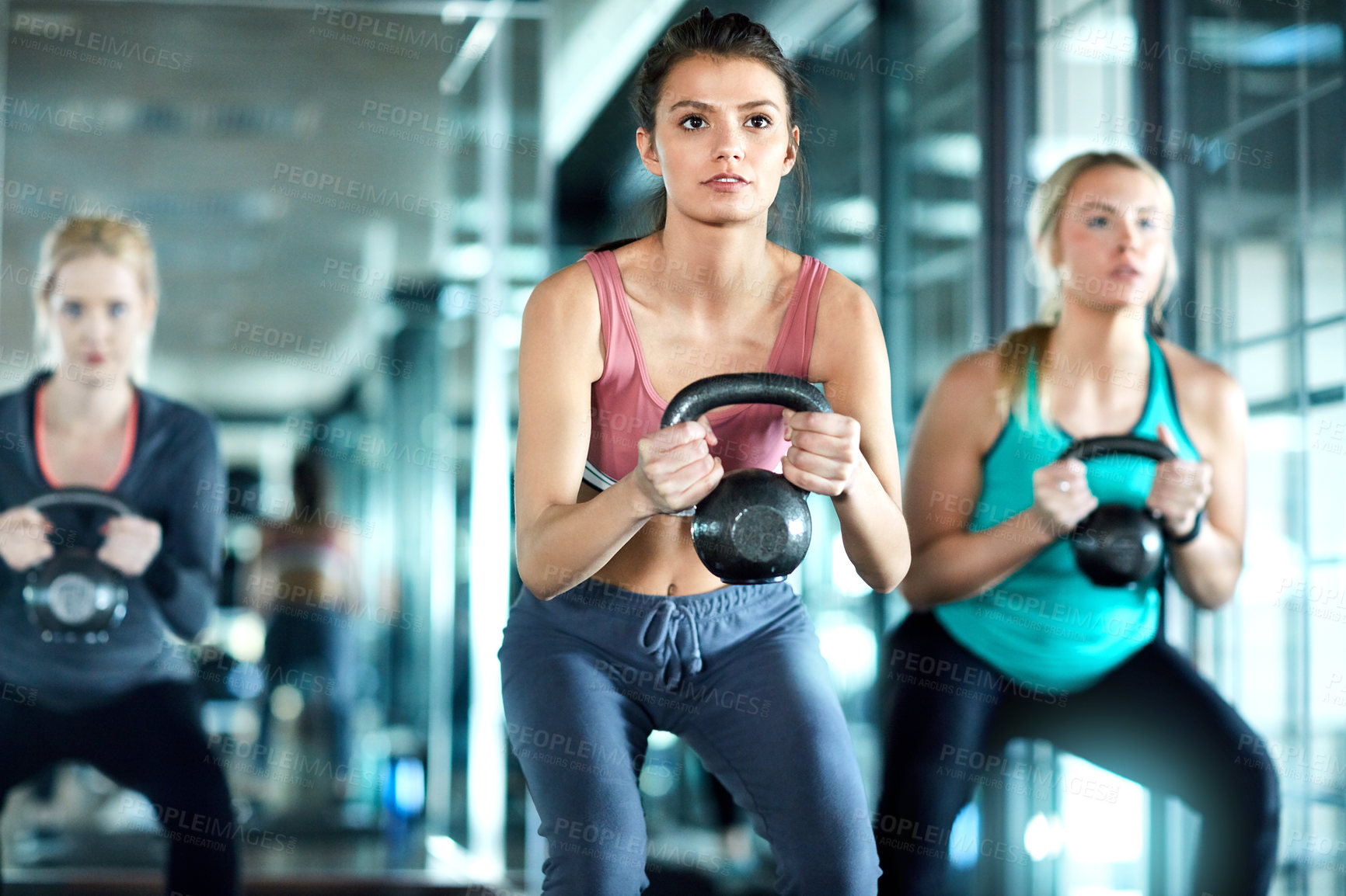 Buy stock photo Shot of three attractive young women working out with kettle bells in the gym