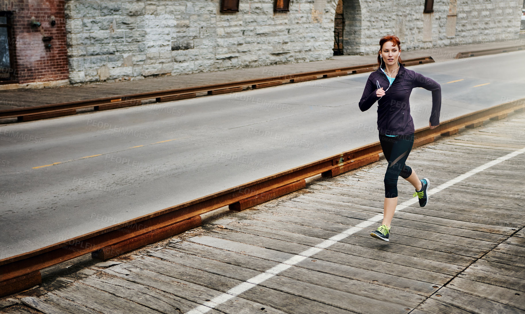 Buy stock photo Shot of a sporty young woman listening to music while running in the city