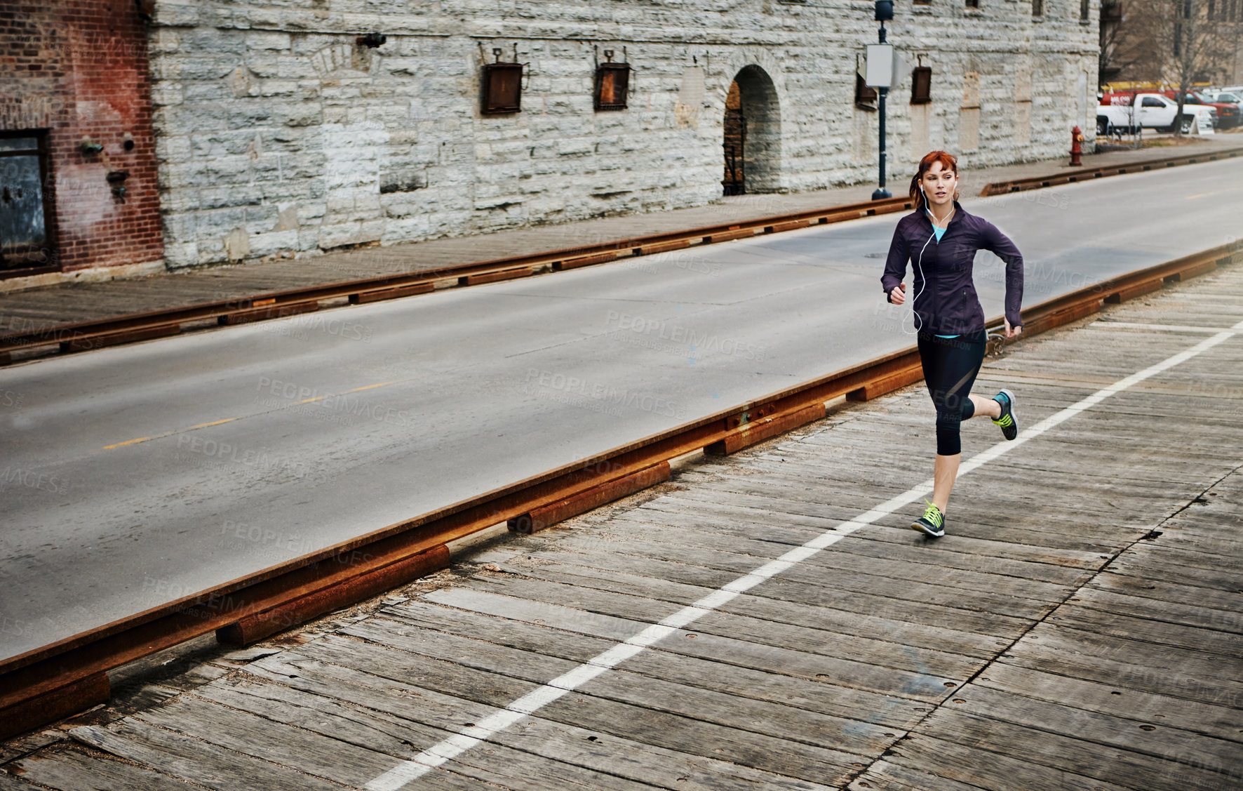 Buy stock photo Shot of a sporty young woman listening to music while running in the city