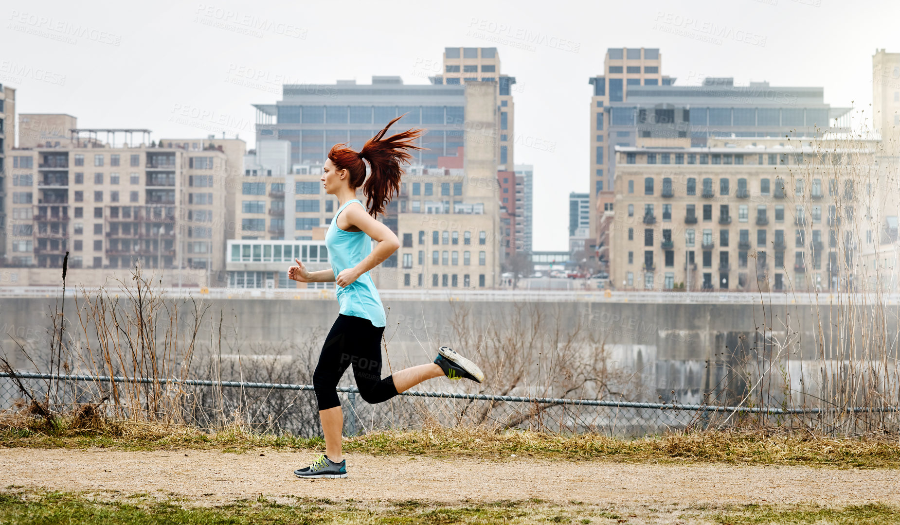 Buy stock photo Shot of a sporty young woman running alongside the city