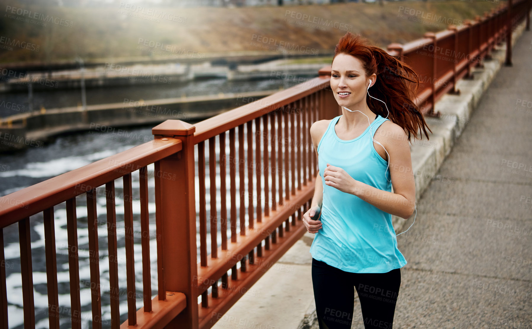 Buy stock photo Shot of a sporty young woman listening to music while running in the city