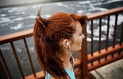 Buy stock photo Shot of a sporty young woman listening to music while out for a run in the city