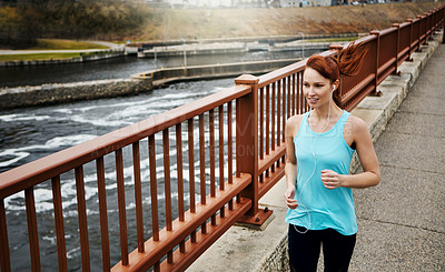 Buy stock photo Shot of a sporty young woman listening to music while running in the city