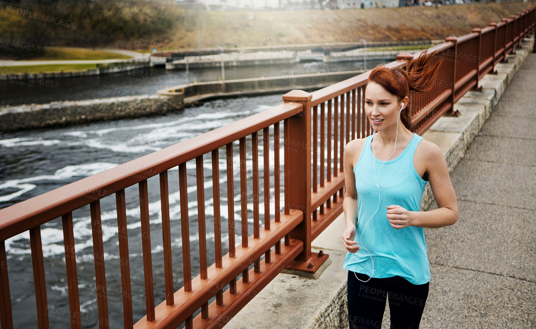 Buy stock photo Shot of a sporty young woman listening to music while running in the city