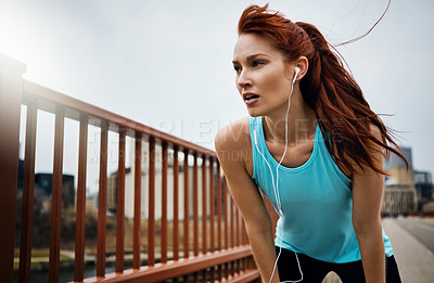 Buy stock photo Shot of a sporty young woman taking a break while running in the city