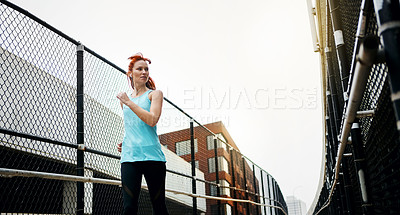 Buy stock photo Shot of a sporty young woman listening to music while running in the city