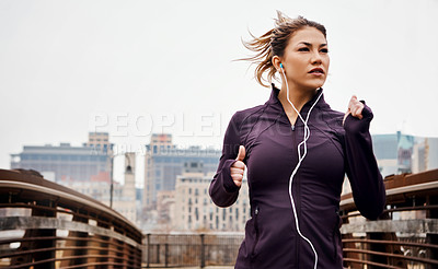 Buy stock photo Cropped shot of an attractive young woman listening to music while running through the city