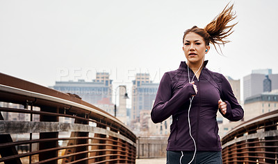 Buy stock photo Cropped shot of an attractive young woman listening to music while running through the city