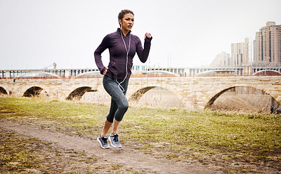 Buy stock photo Full length shot of an attractive young woman listening to music while running alongside the city