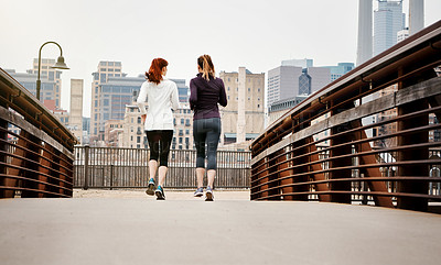 Buy stock photo Rearview shot of two unrecognizable young women running through the city