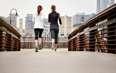 Buy stock photo Rearview shot of two unrecognizable young women running through the city