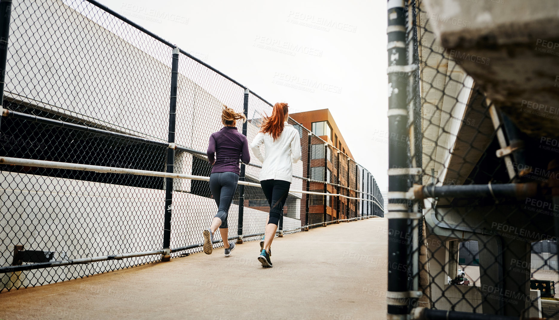 Buy stock photo Rearview shot of two unrecognizable young women running through the city