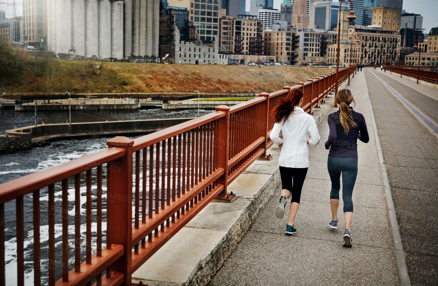 Buy stock photo Rearview shot of two unrecognizable young women running through the city