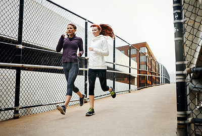 Buy stock photo Full length shot of two attractive young women running through the city