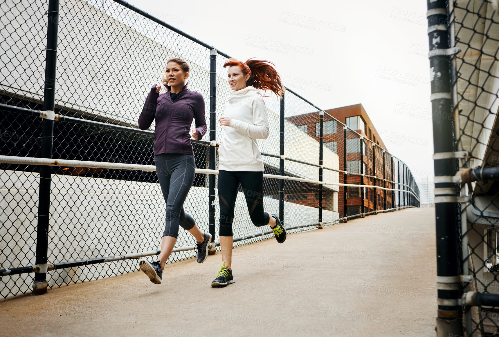 Buy stock photo Full length shot of two attractive young women running through the city