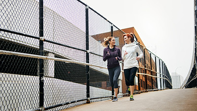 Buy stock photo Full length shot of two attractive young women running through the city