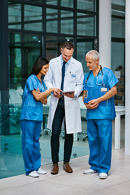 Buy stock photo Shot of a group of medical practitioners working together on a digital tablet in a hospital