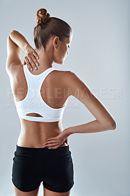 Buy stock photo Studio shot of an athletic young woman holding her neck and back in pain against a grey background