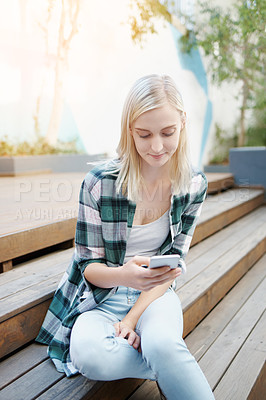 Buy stock photo Shot of a young woman sitting on the steps outside and using a mobile phone