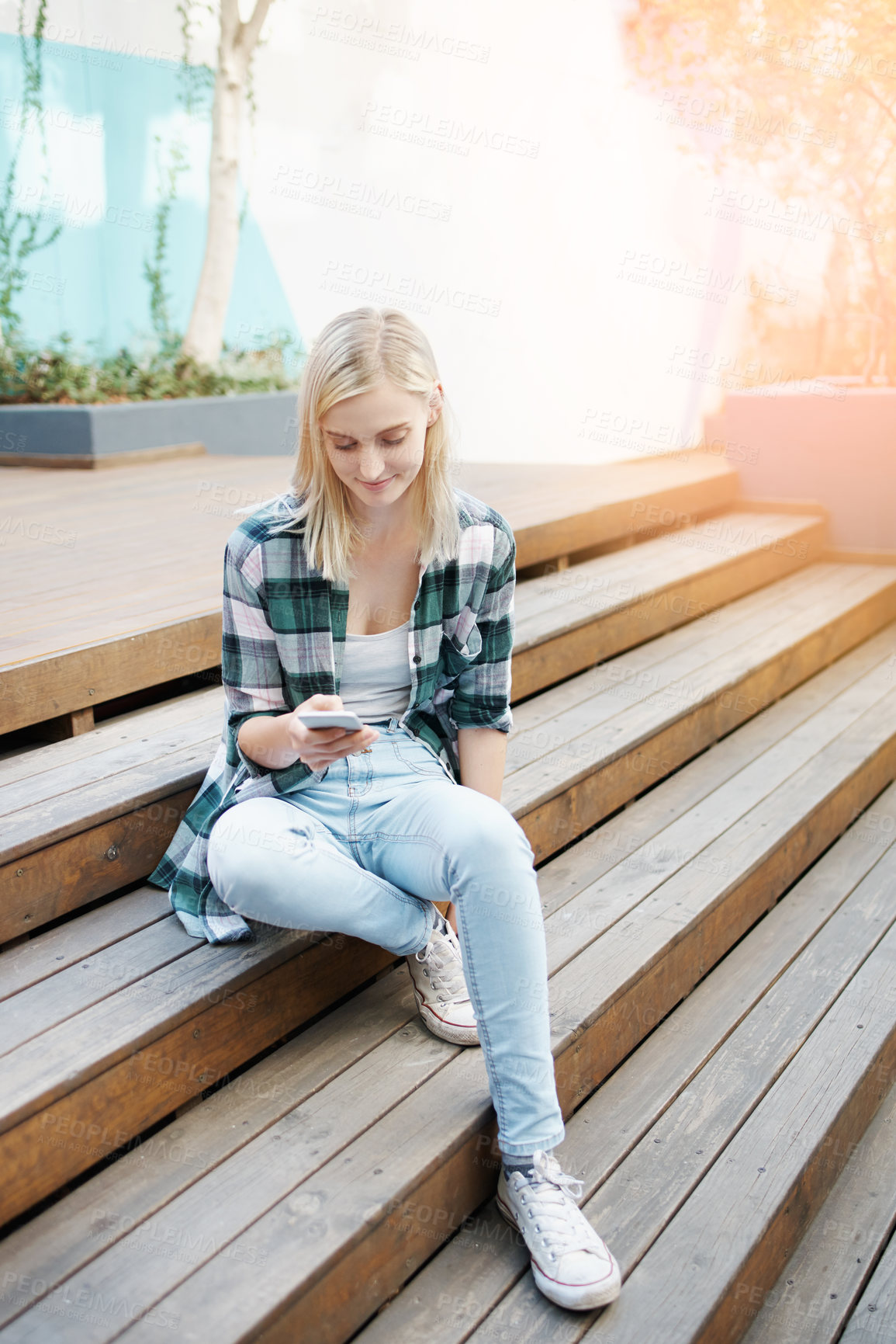 Buy stock photo Shot of a young woman sitting on the steps outside and using a mobile phone