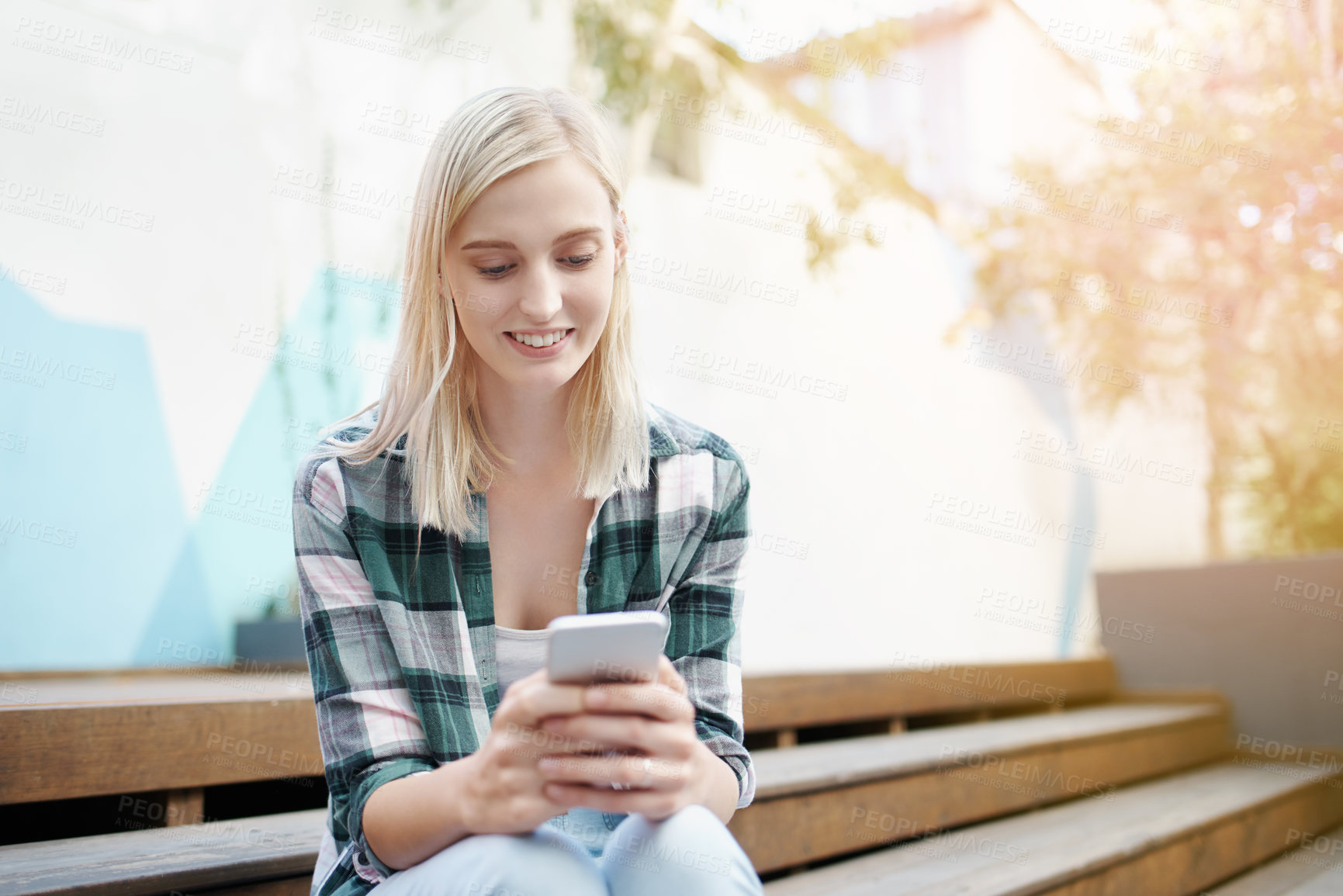 Buy stock photo Shot of a young woman sitting on the steps outside and using a mobile phone