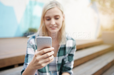 Buy stock photo Shot of a young woman sitting on the steps outside and using a mobile phone
