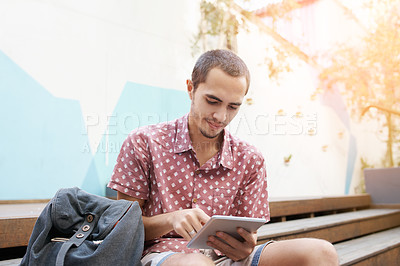 Buy stock photo Shot of a young man sitting on the steps outside on campus and using a digital tablet