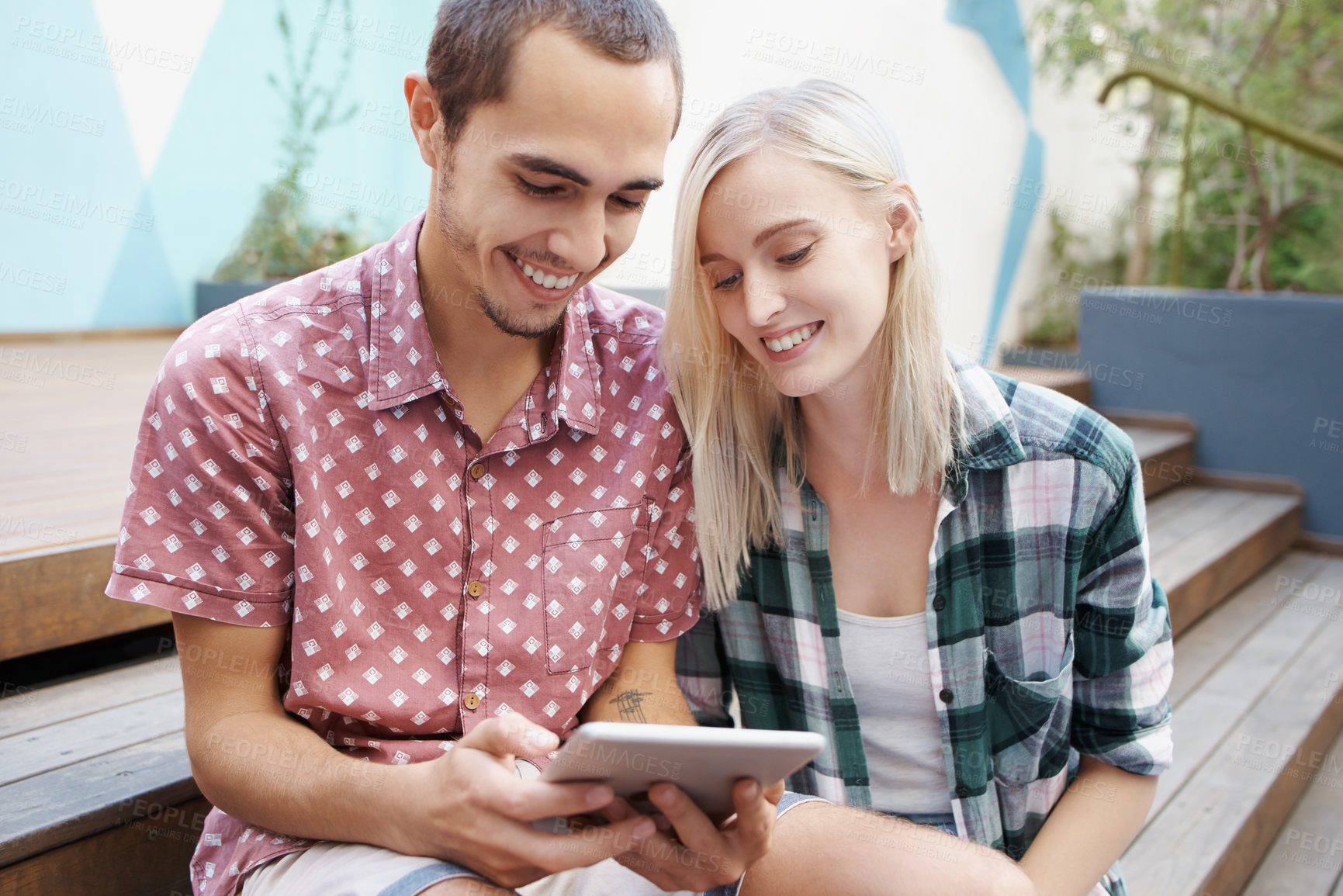 Buy stock photo Shot of a young couple sitting on the steps outside and using a digital tablet together